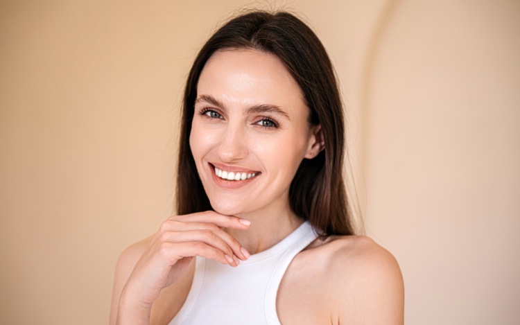 studio shot of young smiling woman with healthy radiant skin looking at camera and touching her chin. eyebrow lamination, skincare concept
